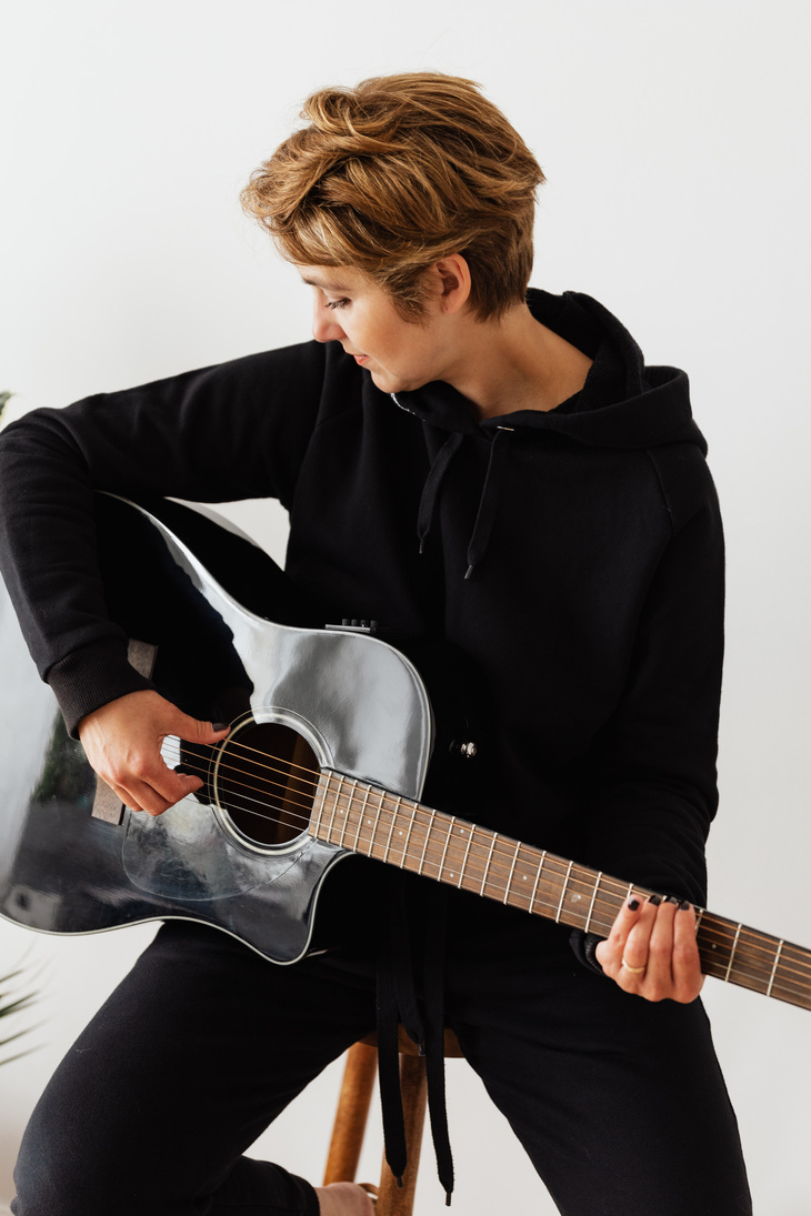 Trendy female musician playing acoustic guitar at home